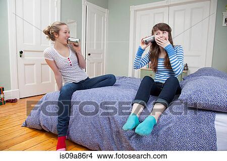Girls sitting on bed playing with tincan telephone View Large Photo Image Picture - Girls sitting on bed playing with tincan telephone. Fotosearch