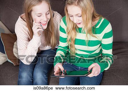 Stock Image - Girls sitting on sofa looking at digital tablet. Fotosearch