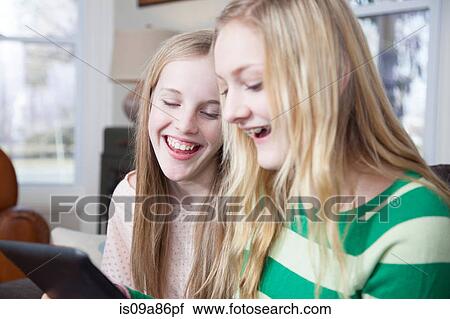 Stock Image - Girls sitting on sofa looking at digital tablet. Fotosearch