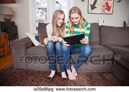 Stock Image - Girls sitting on sofa looking at digital tablet. Fotosearch