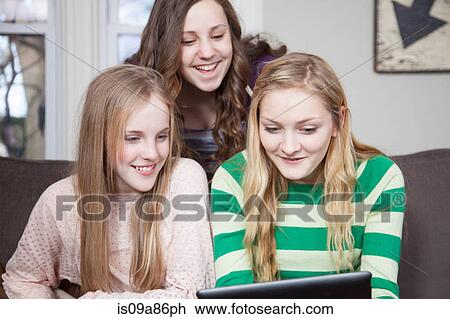 Stock Image - Girls sitting on sofa looking at digital tablet. Fotosearch