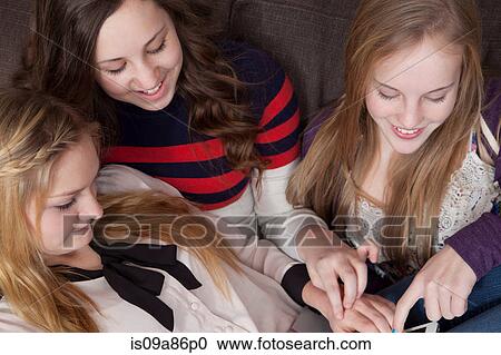 Stock Image - Girls sitting on sofa using digital tablet. Fotosearch