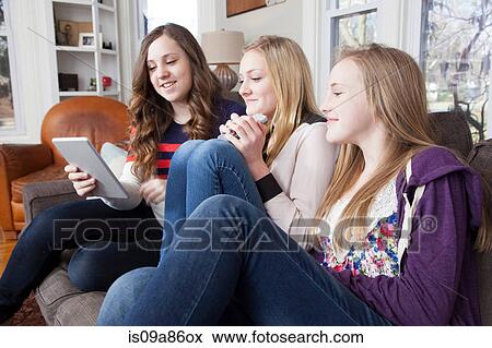 Girls sitting on sofa using digital tablet View Large Photo Image Stock Photo - Girls sitting on sofa using digital tablet. Fotosearch