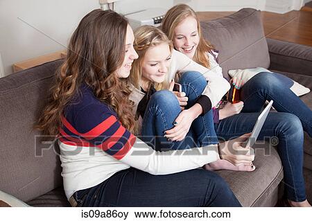 Girls sitting on sofa using digital tablet View Large Photo Image Stock Photo - Girls sitting on sofa using digital tablet. Fotosearch