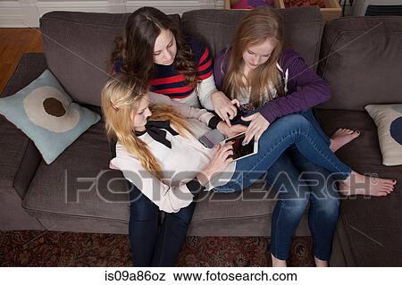Girls sitting on sofa using digital tablet View Large Photo Image Stock Photo - Girls sitting on sofa using digital tablet. Fotosearch
