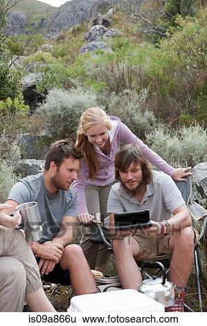 Stock Photograph - Group of young hikers taking a break, looking at hand held computer. Fotosearch
