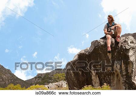 Stock Image - Male hiker sitting on rock formation with drinking flask. Fotosearch
