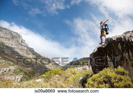 Stock Photo - Male hiker standing on rock formation with arms outstretched. Fotosearch