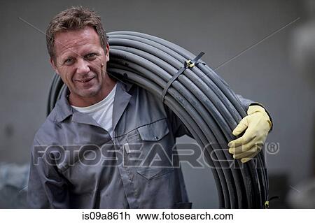 Stock Image - Man carrying reel of cable. Fotosearch