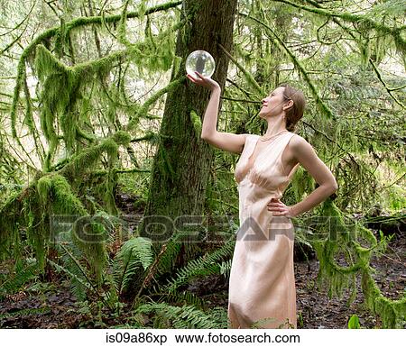 Stock Photography - Mature woman looking into crystal ball in forest. Fotosearch