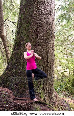 Stock Image - Mature woman performing tree pose in forest. Fotosearch