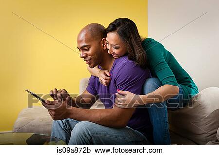 Mid adult couple sitting on sofa looking at digital tablet View Large Photo Image Stock Image - Mid adult couple sitting on sofa looking at digital tablet. Fotosearch