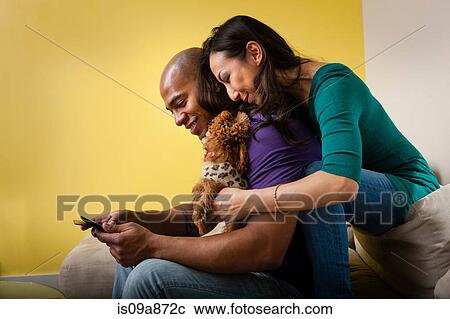 Mid adult couple sitting on sofa with dog and smartphone View Large Photo Image Stock Image - Mid adult couple sitting on sofa with dog and smartphone. Fotosearch