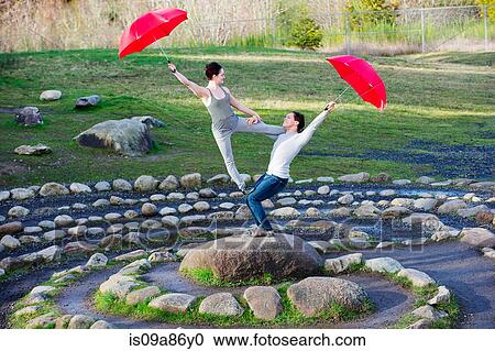 Stock Image - Mid adult dancers performing with red umbrellas in stone circle. Fotosearch