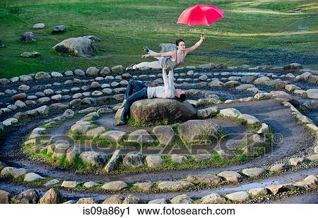 Stock Image - Mid adult dancers performing with red umbrellas in stone circle. Fotosearch