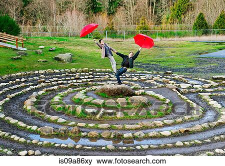 Stock Photo - Mid adult dancers performing with red umbrellas in stone circle. Fotosearch