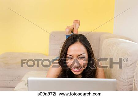 Mid adult female lying on sofa looking at laptop View Large Photo Image Stock Image - Mid adult female lying on sofa looking at laptop. Fotosearch