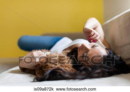 Mid adult female lying on sofa with dog and smartphone View Large Photo Image Stock Image - Mid adult female lying on sofa with dog and smartphone. Fotosearch
