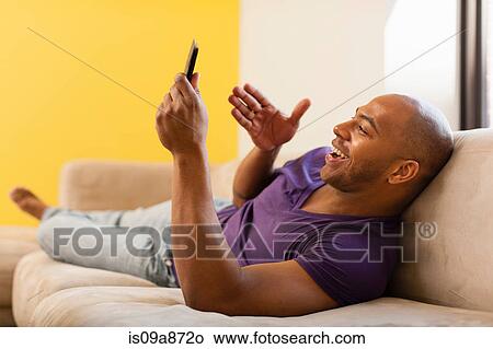 Picture - Mid adult male on sofa using digital tablet. Fotosearch