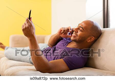 Stock Photography - Mid adult male on sofa using digital tablet and mobile phone. Fotosearch
