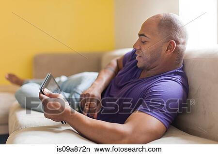 Mid adult male on sofa with digital tablet View Large Photo Image Picture - Mid adult male on sofa with digital tablet. Fotosearch