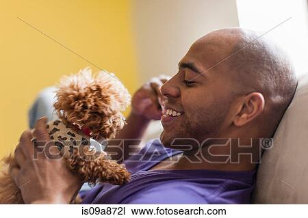 Stock Image - Mid adult male relaxing on sofa with dog. Fotosearch