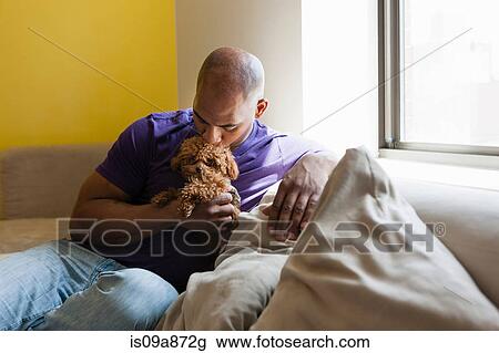 Stock Image - Mid adult male sitting on sofa with dog. Fotosearch