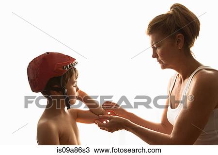 Stock Image - Mother putting adhesive plaster on son's elbow. Fotosearch