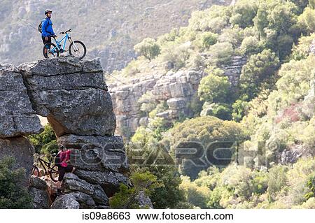 Stock Image - Mountain biking couple on rock formation looking ahead. Fotosearch