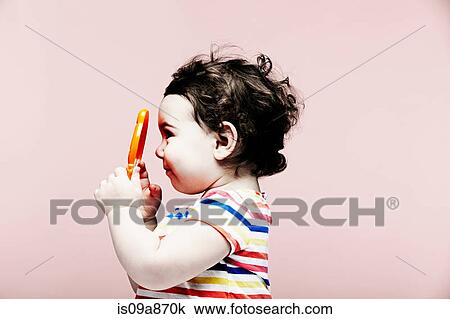 Stock Image - Portrait of baby girl holding plastic toy. Fotosearch