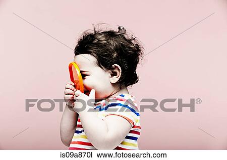 Stock Image - Portrait of baby girl holding plastic toy. Fotosearch