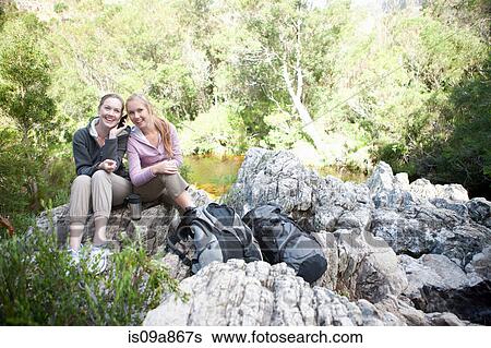 Portrait of girl hikers sitting on rock using cellphone View Large Photo Image Stock Photograph - Portrait of girl hikers sitting on rock using cellphone. Fotosearch