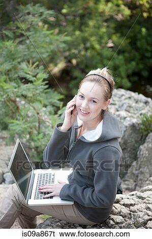 Stock Photograph - Portrait of teenager using laptop and cellphone outdoors. Fotosearch