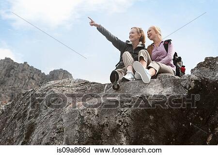 Stock Image - Portrait of two girl hikers sitting on rock formation. Fotosearch