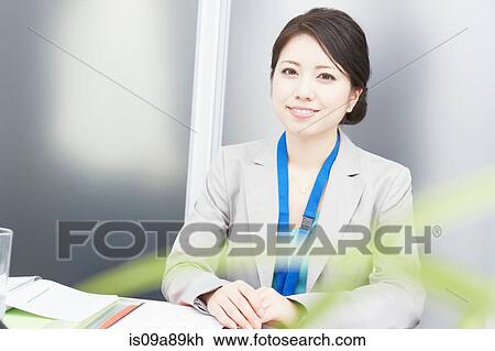 Stock Image - Portrait of woman at desk smiling. Fotosearch