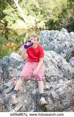 Stock Photography - Portrait of young boy drinking from flask on rock. Fotosearch