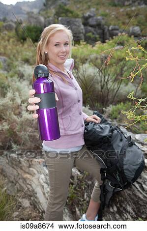 Picture - Portrait of young female hiker holding drinks flask. Fotosearch