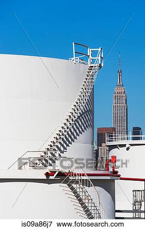 Stock Photo - Storage tanks of oil refinery with Empire State building in background, New York, USA. Fotosearch