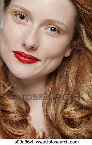 Stock Photograph - Studio shot of young woman with curly red hair wearing make up. Fotosearch