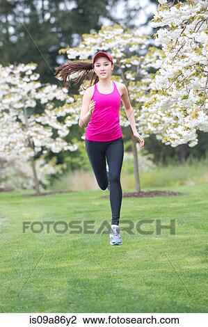 Stock Image - Teenage girl wearing pink sportswear running in park. Fotosearch