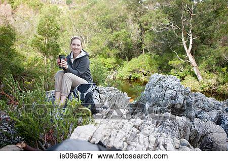 Stock Photography - Teenage hiker drinking from flask on rock. Fotosearch