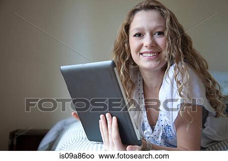 Picture - Teenager on bed, reading digital tablet. Fotosearch