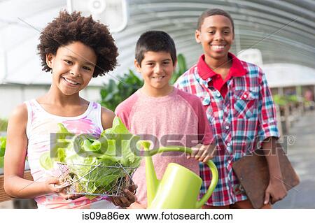 Stock Photo - Three children in greenhouse, boy holding watering can. Fotosearch