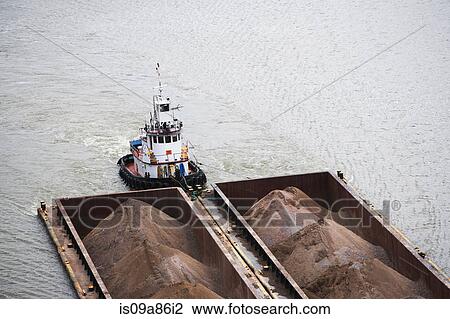 Stock Image - Tugboat pushing barges of sand, high angle view. Fotosearch