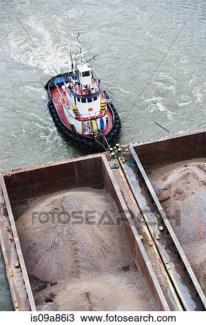 Stock Image - Tugboat pushing barges of sand, high angle view. Fotosearch
