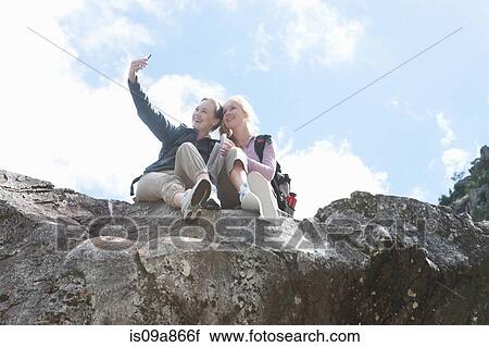 Stock Image - Two girl hikers taking self portrait on top of rock formation. Fotosearch