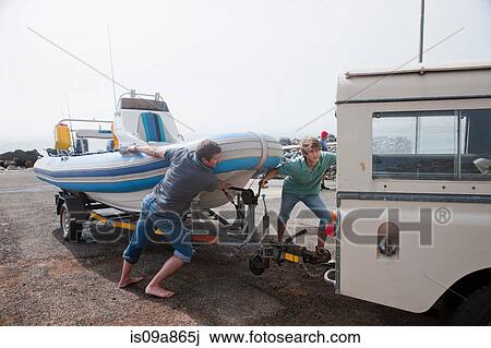 Stock Image - Two young men fixing dinghy trailer to vehicle. Fotosearch