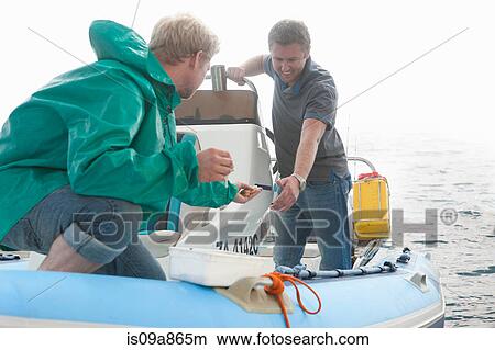 Picture - Two young men looking at fishing bait in dinghy. Fotosearch