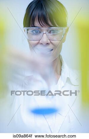 Stock Image - Woman holding up laboratory beaker. Fotosearch