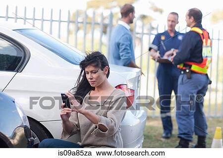 Stock Image - Woman photographing damage on her car at car accident scene. Fotosearch
